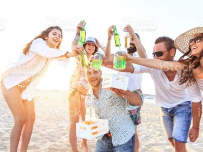Group of friends having fun on beach and drinking beer, celebrating.
